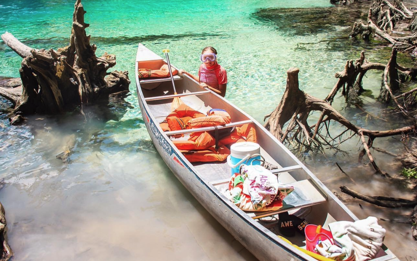 a small girl standing next to a canoe full of gear
