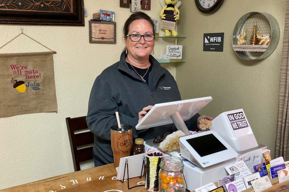 the shop owner, standing behind a checkout register, smiling at the camera