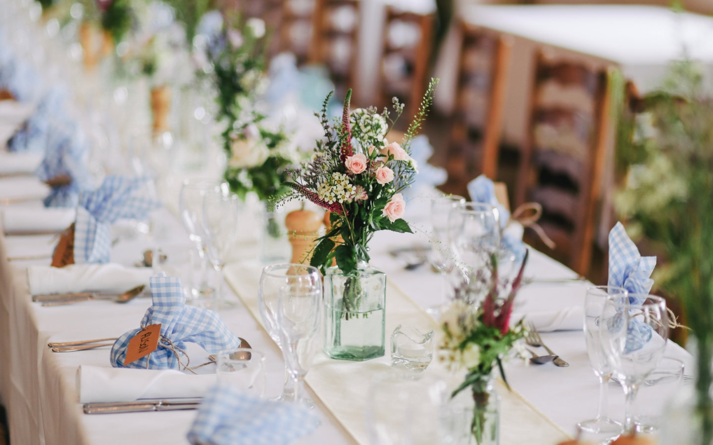 a reception table with wooden chairs, floral table decorations, wine glasses