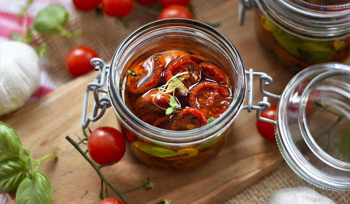 mason jar of tomatoes on a kitchen table with fresh tomatoes, basil and garlic sitting around it